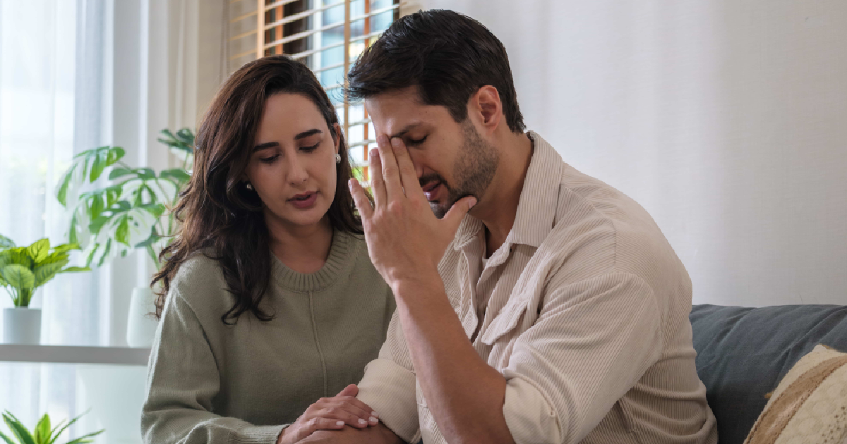 A concerned couple sits together on a couch, with the man appearing distressed and holding his head representing emotional struggles related to Low testosterone (Low-T) in Webster, TX.